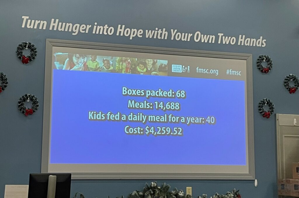 A picture of a screen that has statistics on it for how many boxes packs, meals made, kids fed a daily meal for a year, and cost for the Feed My Starving Children volunteer event.