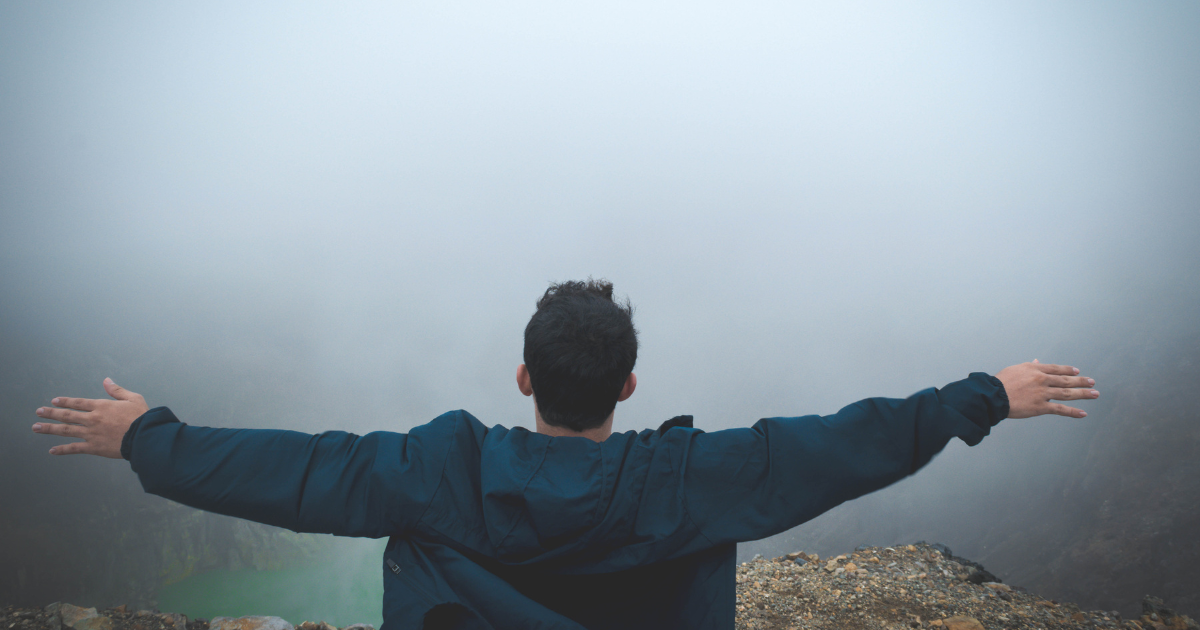 Photograph of a man standing on a mountaintop with his arms completely outstretched to illustrate how financial freedom feels.