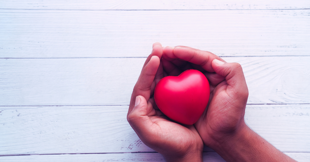 Two hands cupping a red heart against a white wooden background to illustrate giving to charity through the use of a donor-advised fund.