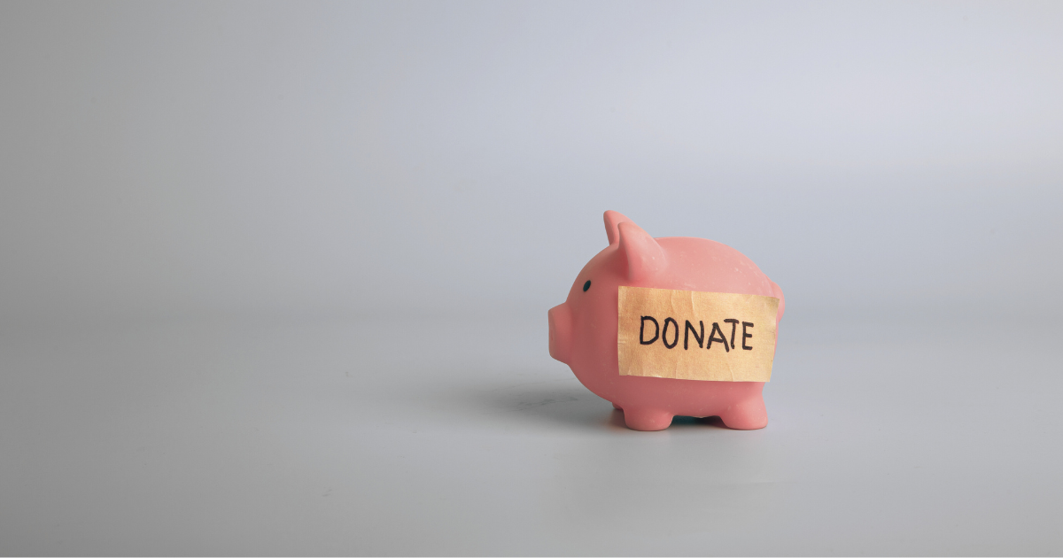 Pink pig toy on a gray background with a piece of tape across it's body with DONATE written in black marker. This image represents charitable giving.